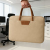 A tan suede PU leather laptop bag with brown handles is being held in an office setting. It features a logo.