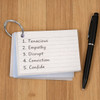 A set of A7 index cards with a ring, featuring a list of words, alongside a black pen on a wooden surface.