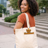 A woman with curly hair smiles while carrying a cream-coloured tote bag with a logo.