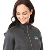 A woman in a grey softshell jacket with a logo, featuring a high collar and zippered pockets.