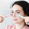 A woman using a double-headed ice massager roller in pink and blue, applying it to her face.