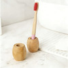 A bamboo toothbrush stand in natural wood tones, featuring two holders with a toothbrush placed in one.
