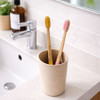 A cup holds two large conical handle toothbrushes, one yellow and one pink, on a bathroom counter.