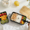 A black expandable lunch box contains grilled chicken, rice, cherry tomatoes, and a side compartment with strawberries, kiwifruit, and orange.