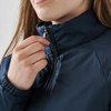 A close-up of a woman's hand adjusting the zipper of a navy thermal jacket with a high collar.