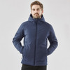 A man wearing a navy puffer jacket with a hood, featuring a branding logo. The jacket has a sleek, modern design.