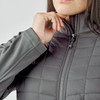 A women's grey softshell jacket featuring a quilted design and a zippered front. It has a logo on the chest.