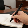 A black plastic pen with a textured grip is held above an open notebook on a desk.