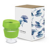 A drink bottle with a clear body and a green lid, displayed with a decorative box featuring floral patterns.