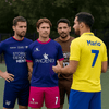 Four players in various colourful soccer jerseys: blue, purple, brown, and yellow, standing on a field.