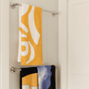 A yellow bath towel with a pattern hangs above a black towel featuring a design, both on a towel rack.