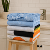 A stack of bath sheets in various colours, including blue, grey, orange, and white, on a wooden stool.