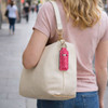 A beige bag hung on a woman's shoulder, featuring a pink leopard-print neoprene lipstick bag attached.