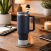 A drink bottle with a navy blue silicone straw cover shaped like a bucket hat, sitting on a wooden table.