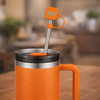 A drink bottle with an orange silicone straw cover and a stainless steel straw, placed on a blurred background.