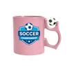 A pink ceramic mug with a soccer-themed logo and a soccer ball-shaped handle. It includes a branding logo.