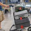 A luggage trolley loaded with grey and black suitcases, each featuring a soft silicone luggage tag in red.