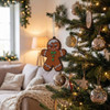 A gingerbread man decoration hangs from a Christmas tree, adorned with baubles and festive lights in a cozy living room.