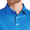 A close-up of a men's blue polo shirt featuring a tonal dot print and a logo on the collar.