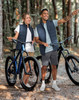 A pair of models wearing navy insulated puffer vests, standing beside bicycles in a forest setting.