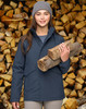 A woman in a navy quilted waterproof jacket holds logs, standing in front of a stacked woodpile. The jacket features a hood.