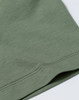 A close-up of a sage green cotton short-sleeve tee shirt featuring a stitched hem and a subtle logo.