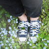 A pair of navy shoes adorned with colourful custom shoe charms, surrounded by small blue flowers and green grass.