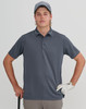 A young man in a grey polo shirt and cap holds a golf club, wearing a golf glove. The background is neutral.
