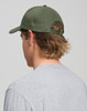 A green cotton twill unstructured cap viewed from the back on a person with long hair, wearing a grey shirt.