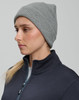 A grey roll-up cable knit snug beanie displayed on a model, wearing a dark jacket. The beanie has a logo.