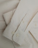 A light beige cotton blend long-sleeve shirt featuring buttoned cuffs and a smooth fabric texture.