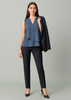 A woman wearing a sleeveless blue top and slim leg black pants, holding a black blazer.