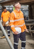 A bright orange men's work shirt with segmented tape, paired with navy pants, worn by a worker on site.