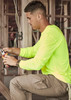A man works in a construction setting, wearing a neon yellow long sleeve tee and beige cargo pants, using pliers.