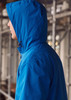 A blue unisex super light packable rain jacket with a hood, featuring a logo, displayed on a model from the side.