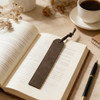 A vintage style high-quality bookmark in brown leather resting on an open book, accompanied by a cup of coffee.