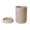 A beige ceramic coffee cup with a matching lid, featuring a simple cylindrical design and a logo.