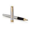 A brushed stainless steel rollerball pen with a gold trim and a black writing tip, featuring a logo.