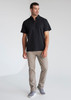 A man wearing a black short sleeve polo shirt and light grey trousers, featuring a logo on the polo.