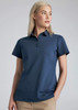 A woman models a navy blue short sleeve polo shirt with a collar and a logo on the chest.
