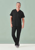 A man poses in black unisex scrub pants and matching short-sleeve top, with a plain background.