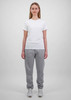 A woman wears a plain white t-shirt and grey track pants, standing against a light grey background. The pants have a logo.