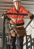A unisex hi-vis full zip stretch taped hoodie in bright orange, worn by a person holding a power tool while on scaffolding.