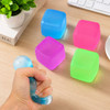 A hand squeezing a blue squishy stress relief cube among pink, green, and blue cubes on a wooden desk.