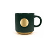 A ceramic coffee mug in dark green with a bronze circular accent and ribbed texture, featuring a logo.