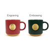 A red ceramic coffee mug with a bronze medal and a green ceramic coffee mug with a bronze medal, both ribbed.