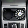 An air freshener in a circular black holder, placed in a car cup holder, featuring a logo.