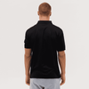A black polo shirt is displayed from the back, featuring a collar and short sleeves. It has a logo on the upper back.