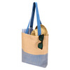 A tote bag in beige and blue with long handles, featuring a pair of sunglasses and round items inside.