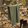 A green Frontier Rapid Dry Towel hangs from a camping chair beside a fire, with boots on the ground nearby.